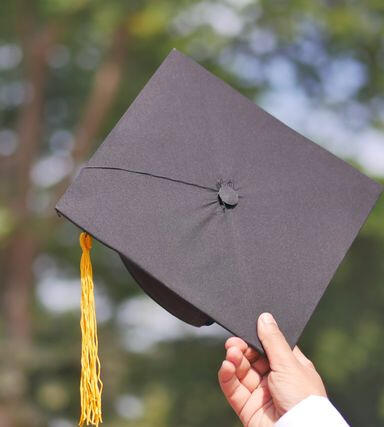 A hand holding a graduate cap with a yellow tassle.