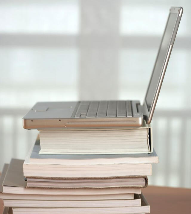 A laptop stacked on a pile of books.